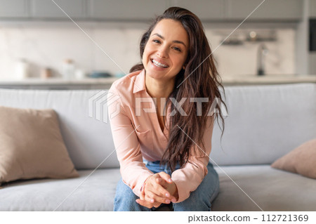 Cheerful woman sitting on grey couch, smiling 112721369