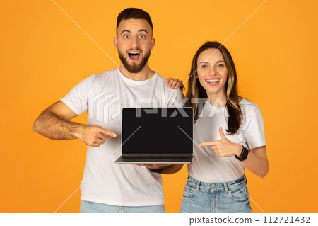 Excited young couple presenting a laptop with a blank screen, perfect for advertising 112721432