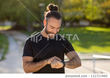 Athletic man wearing activewear monitors his workout with smartwatch outdoors 112721460