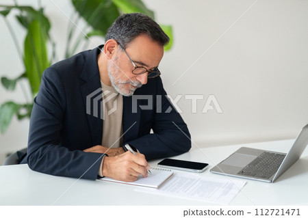 Concentrated senior professional in glasses and a business suit diligently taking notes 112721471