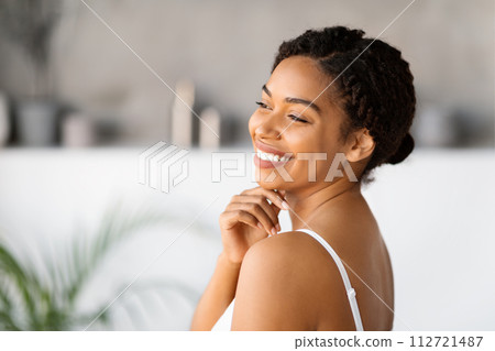 Happy young black woman wearing white tank top smiling and touching chin 112721487