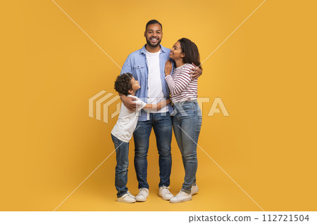 Family Warmth. African American Father, Mother And Son Embracing Against Yellow Background Family Warmth. African American Father, Mother And Son Embracing Against Yellow Background 112721504