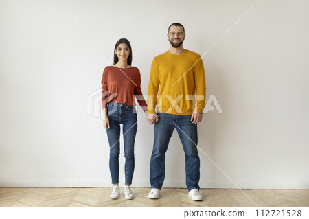Happy young couple in casual clothes holding hands and smiling at camera Happy young couple in casual clothes holding hands and smiling at camera 112721528