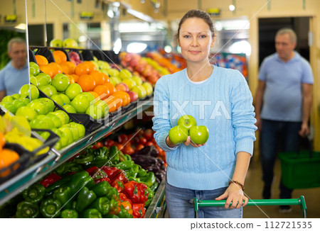 Positive middle-aged female buyer choosing organic granny smith green apples in hypermarket 112721535