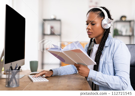 Focused black female student with headphones reviewing notes while using computer 112721545