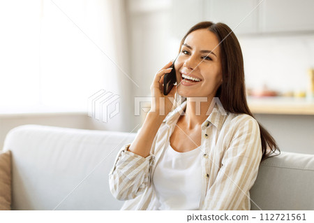 Delighted young woman enjoying pleasant conversation on her mobile phone at home Delighted young woman enjoying pleasant conversation on her mobile phone at home 112721561