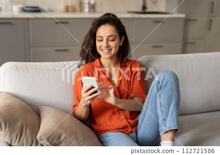 Joyful young woman texting on smartphone at home 112721586