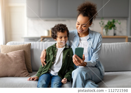 Smiling black mom and son enjoying smartphone content together 112721598