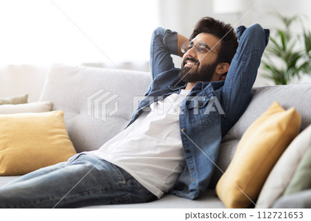 Home Rest. Smiling Dreamy Indian Guy Leaning Back On Comfortable Couch Home Rest. Smiling Dreamy Indian Guy Leaning Back On Comfortable Couch 112721653