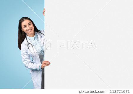 Smiling woman doctor with blank ad board on blue backdrop 112721671
