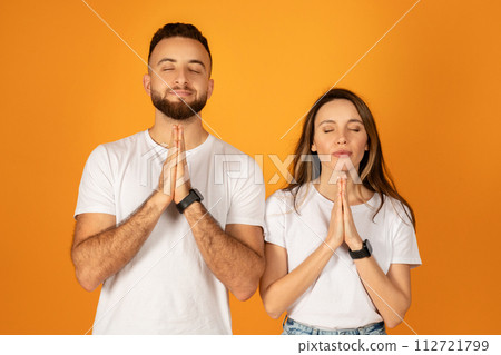 Peaceful young man and woman with eyes closed, hands pressed together in a prayer or meditative pose Peaceful young man and woman with eyes closed, hands pressed together in a prayer or meditative pose 112721799