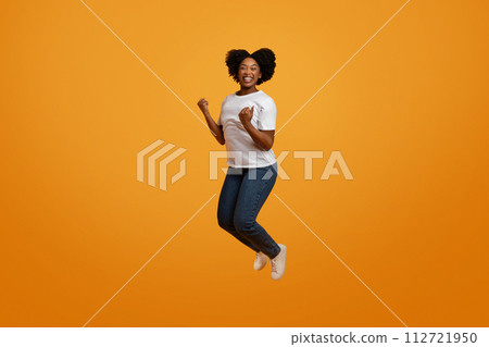 Excited young african american lady jumping in the air Excited young african american lady jumping in the air 112721950