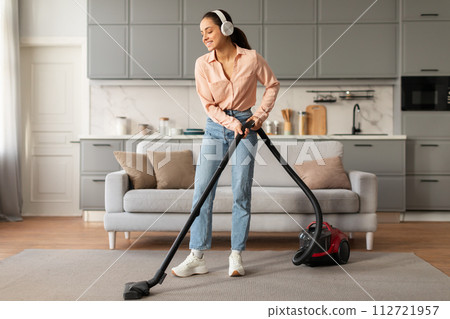 Content woman vacuuming with headphones in neat room Content woman vacuuming with headphones in neat room 112721957