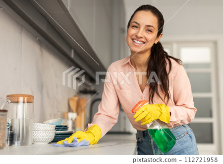 Cheerful woman cleaning kitchen with spray bottle 112721958
