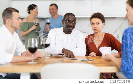 Group of men and women enjoying convivial dinner at kitchen table while playing poker in company of friendly individuals. Idea of evening entertainment concept 112721979