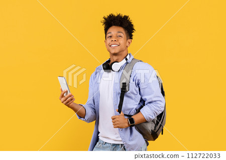 Joyful black male student with headphones and phone on yellow background Joyful black male student with headphones and phone on yellow background 112722033
