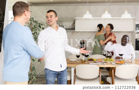 Two men smiled and greeted each other with a firm handshake before taking their seats at beautifully set dinner table Two men smiled and greeted each other with a firm handshake before taking their seats at beautifully set dinner table 112722036