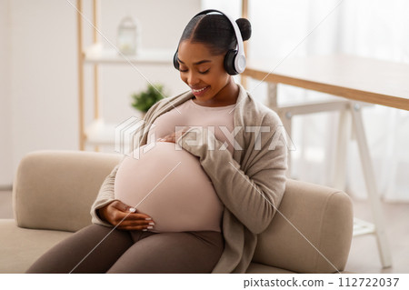 Positive expecting black woman enjoying music at home 112722037