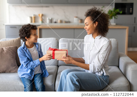 Happy black mother gifting present to her excited son on couch 112722044