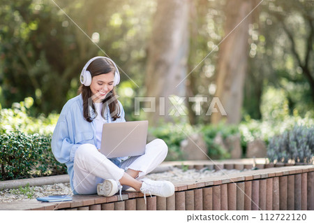 A content young woman enjoys learning on her laptop outdoors, surrounded by nature A content young woman enjoys learning on her laptop outdoors, surrounded by nature 112722120