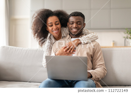 Black couple hugging while using their laptop computer at home 112722149