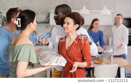 Couple welcoming friends bringing dish for friendly dinner Couple welcoming friends bringing dish for friendly dinner 112722215