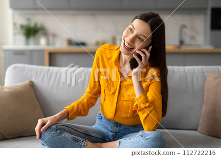 Happy woman chatting on phone, relaxed on couch 112722216