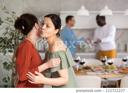Smiling woman giving greeting kiss to bestie at informal dinner Smiling woman giving greeting kiss to bestie at informal dinner 112722227