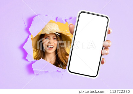 Radiant young woman in a straw hat smiling through a torn purple and yellow paper 112722280