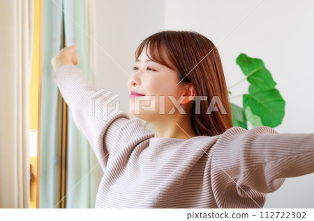 Young woman basking in the morning sun by the window Young woman basking in the morning sun by the window 112722302