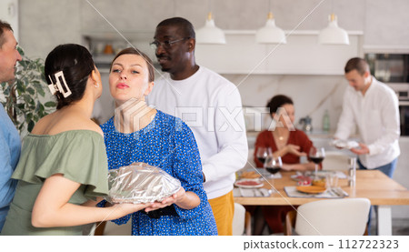 Hostess givng welcoming kiss to female friend bringing dish to party Hostess givng welcoming kiss to female friend bringing dish to party 112722323