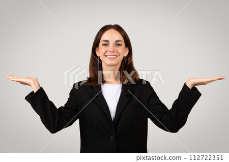 Cheerful businesswoman with brown hair in a black suit comparing invisible items in both hands Cheerful businesswoman with brown hair in a black suit comparing invisible items in both hands 112722351