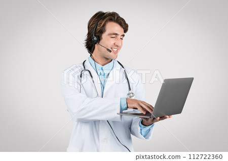 Smiling man doctor with headset using laptop for telehealth services 112722360