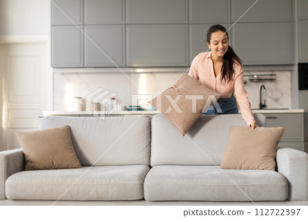 Happy lady arranging pillows on stylish couch at home Happy lady arranging pillows on stylish couch at home 112722397