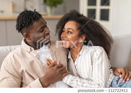 Happy black young couple cuddling sharing embrace in living room Happy black young couple cuddling sharing embrace in living room 112722411
