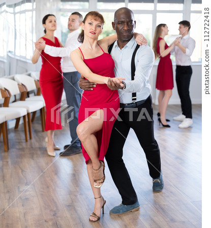 African American man nd woman in red rehearsing elegant tango in pair African American man nd woman in red rehearsing elegant tango in pair 112722418