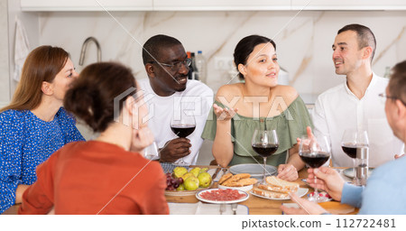 Cheerful adult friends dining and chatting in home kitchen Cheerful adult friends dining and chatting in home kitchen 112722481