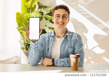 Cheerful young man with curly hair and glasses showing a smartphone screen Cheerful young man with curly hair and glasses showing a smartphone screen 112722506