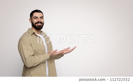 Affable young man with a full beard, gesturing with both hands open as if presenting or welcoming Affable young man with a full beard, gesturing with both hands open as if presenting or welcoming 112722552