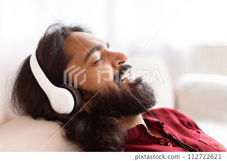 Closeup relaxed indian man reclining on couch, listening to music 112722621
