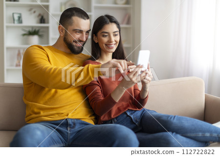 Happy young man and woman using smartphone while relaxing on couch together 112722822