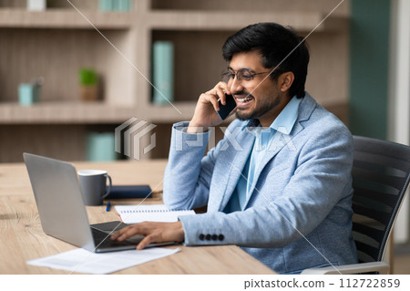 Indian businessman engaging in conversation on phone working online indoor 112722859