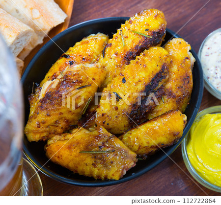 Fried chicken wings served in black bowl, fresh sauses on table Fried chicken wings served in black bowl, fresh sauses on table 112722864