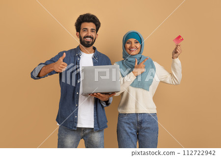 Online banking. Happy muslim couple using laptop and pointing at credit card 112722942