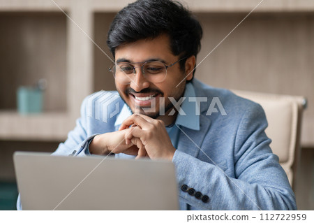 Hindu professional businessman wearing eyeglasses looking at laptop in office Hindu professional businessman wearing eyeglasses looking at laptop in office 112722959