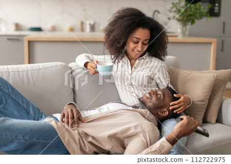 Relaxed African American couple cuddling on sofa in living room Relaxed African American couple cuddling on sofa in living room 112722975