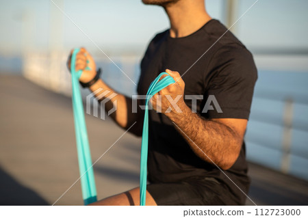 Unrecognizable sporty man doing lunge with resistance rubber band outdoor 112723000