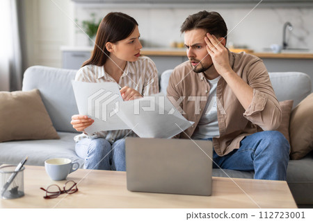 Worried couple reviewing finances with laptop and papers 112723001