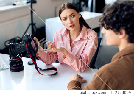Female photographer reviews images with male model during studio shoot 112723009