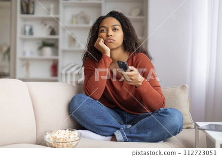 Black woman with remote controller looking bored while watching TV at home Black woman with remote controller looking bored while watching TV at home 112723051